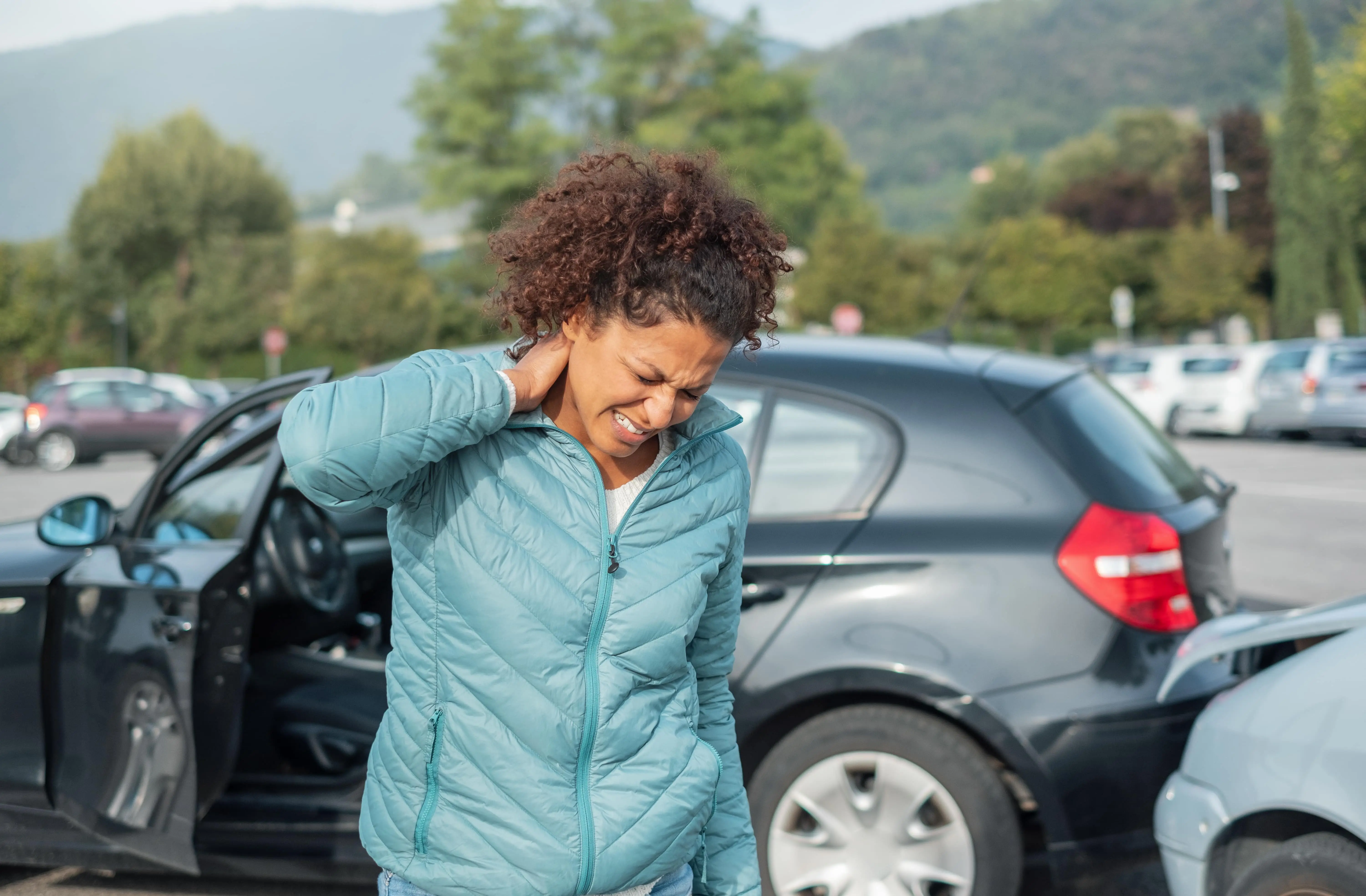 woman who needs a kansas city car accident lawyer holding neck with two sedans crashed into each other in background